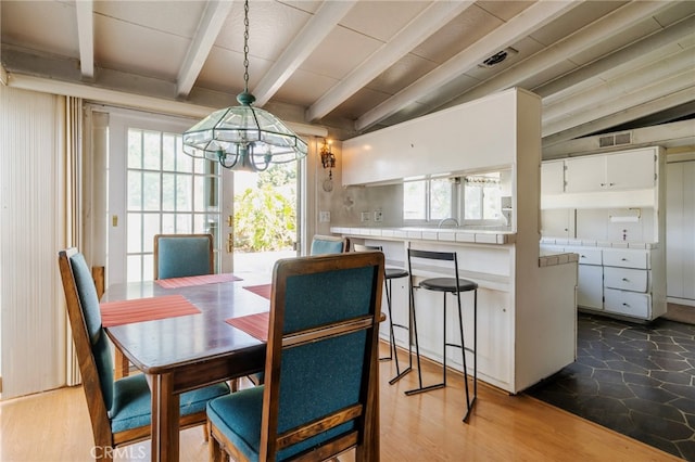 dining space with wood finished floors, visible vents, lofted ceiling with beams, and an inviting chandelier