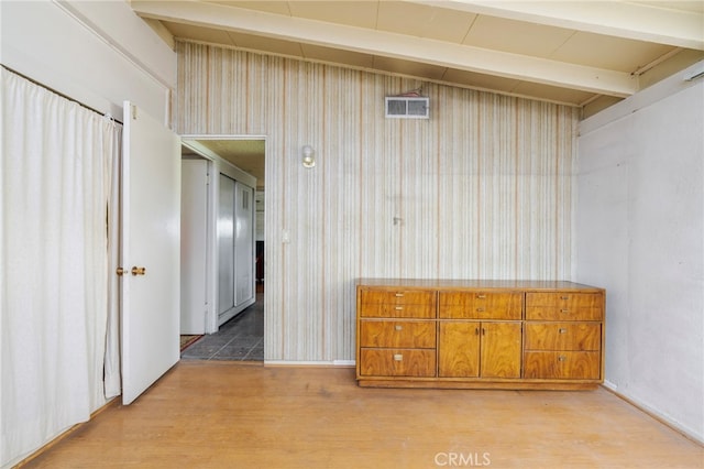 unfurnished bedroom with visible vents, beamed ceiling, wooden walls, and light wood finished floors