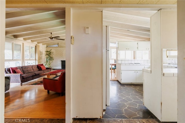 hall with lofted ceiling with beams, stone finish flooring, and plenty of natural light