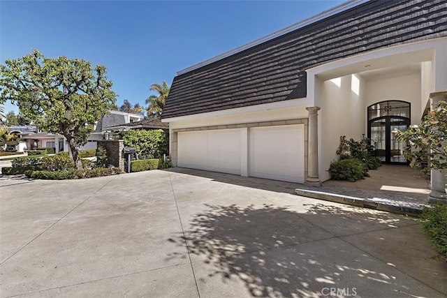 view of side of property with concrete driveway, french doors, mansard roof, and stucco siding