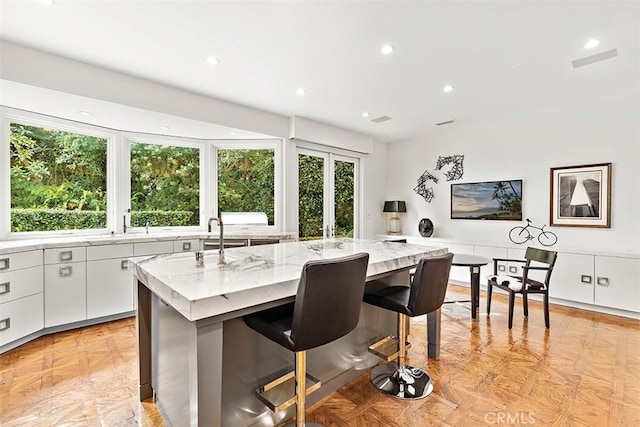 kitchen featuring light stone counters, a center island with sink, recessed lighting, white cabinets, and a kitchen breakfast bar