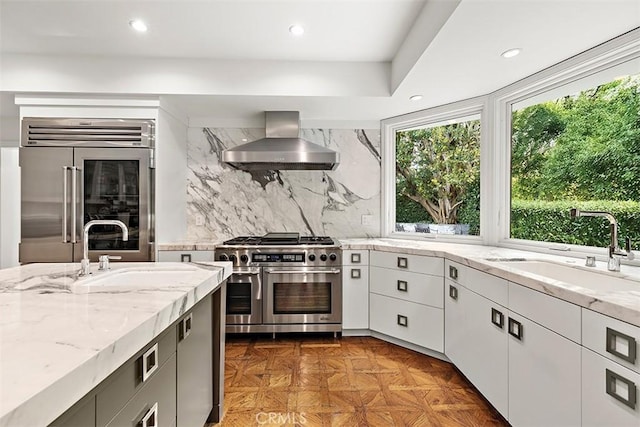 kitchen with wall chimney range hood, high quality appliances, decorative backsplash, and a sink