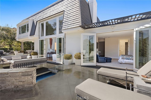 rear view of house featuring a patio area, mansard roof, a chimney, and an outdoor living space