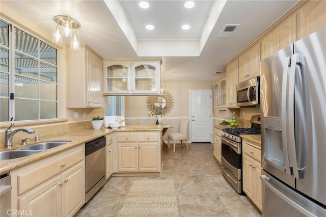 kitchen featuring light brown cabinets, a sink, visible vents, appliances with stainless steel finishes, and glass insert cabinets