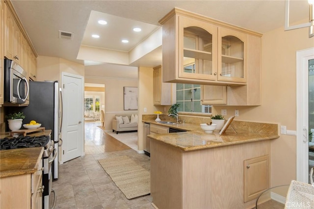 kitchen with light brown cabinetry, appliances with stainless steel finishes, a peninsula, and a sink