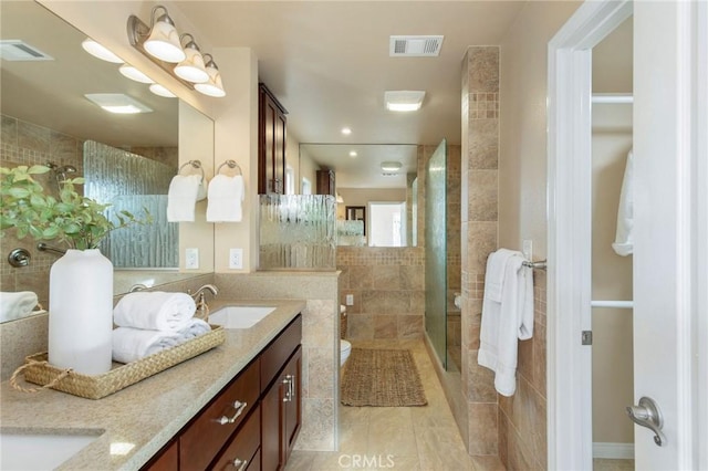 full bath with double vanity, visible vents, a sink, a shower stall, and tile walls