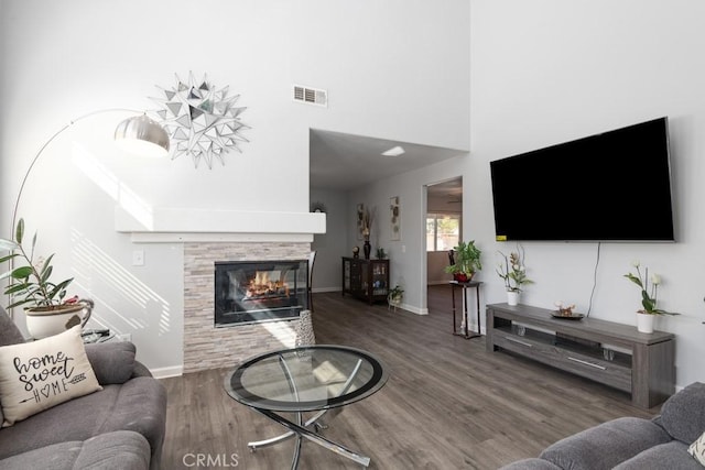 living area featuring baseboards, visible vents, a towering ceiling, wood finished floors, and a multi sided fireplace