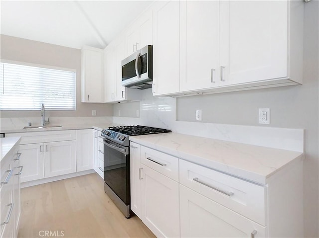 kitchen with stainless steel appliances, a sink, white cabinetry, and light stone countertops