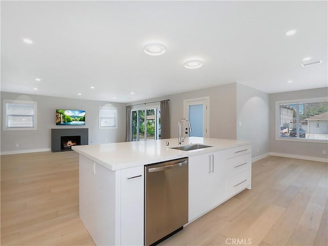 kitchen featuring visible vents, an island with sink, a lit fireplace, stainless steel dishwasher, and a sink