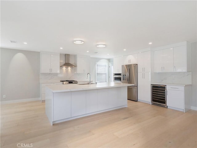 kitchen with beverage cooler, stainless steel appliances, a sink, white cabinets, and wall chimney range hood