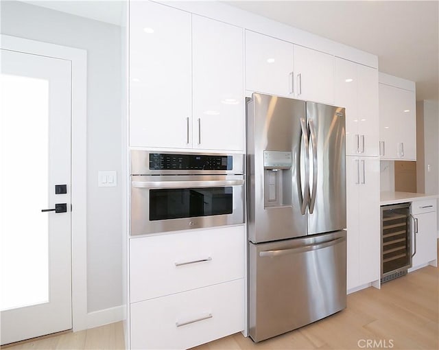 kitchen with wine cooler, stainless steel appliances, light countertops, light wood-style floors, and white cabinets