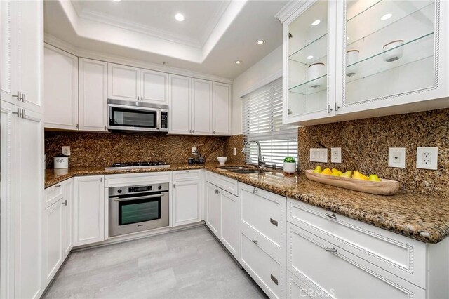 kitchen with a sink, ornamental molding, stainless steel appliances, white cabinetry, and a raised ceiling