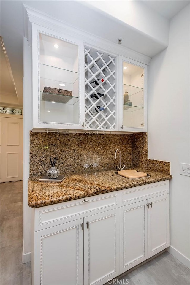 bar with a sink, baseboards, wet bar, and backsplash