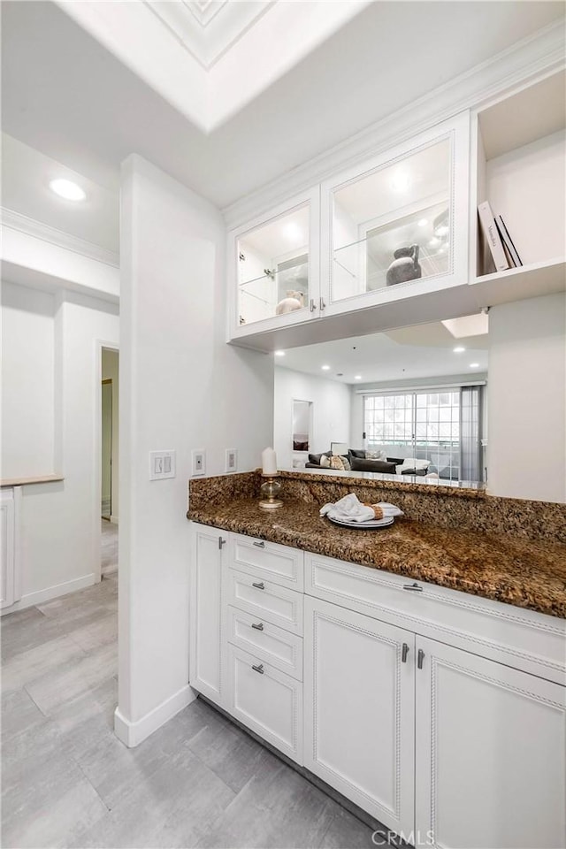 kitchen with dark stone countertops, white cabinetry, recessed lighting, glass insert cabinets, and baseboards