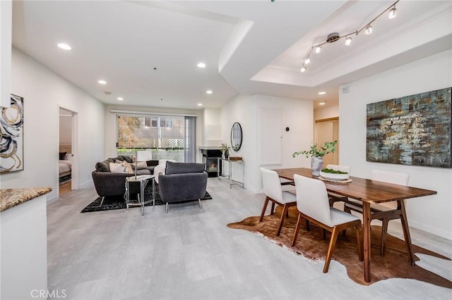 dining room featuring a lit fireplace, a raised ceiling, rail lighting, and recessed lighting