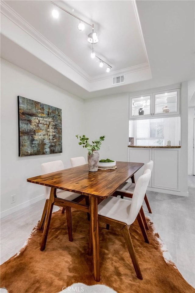 dining room featuring visible vents, baseboards, a tray ceiling, track lighting, and crown molding