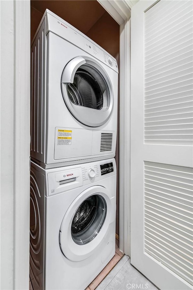 laundry room featuring light tile patterned flooring, laundry area, and stacked washer / dryer