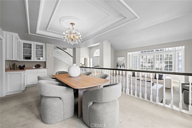 dining space with stairs, a tray ceiling, a notable chandelier, and light carpet