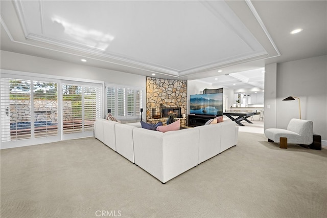 carpeted living area featuring recessed lighting, a tray ceiling, a stone fireplace, and ornamental molding