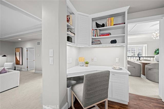 carpeted office space featuring visible vents, baseboards, a chandelier, ornamental molding, and wood finished floors