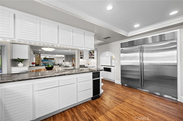 kitchen with visible vents, dark wood-style flooring, white cabinets, built in fridge, and crown molding