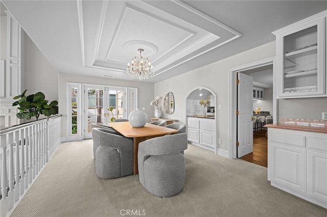 carpeted dining area with a tray ceiling, french doors, arched walkways, and a chandelier