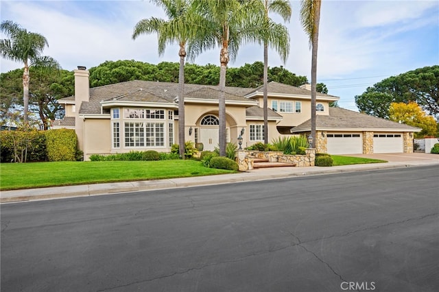 view of front of home featuring stucco siding, a chimney, a front lawn, concrete driveway, and a garage