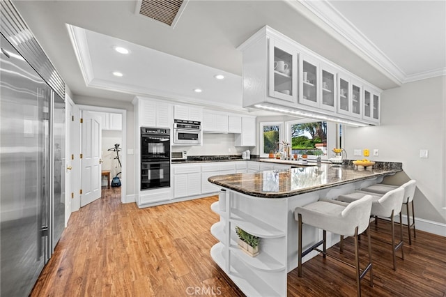 kitchen featuring visible vents, ornamental molding, dobule oven black, built in fridge, and a peninsula