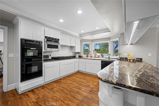 kitchen featuring black appliances, a sink, wood finished floors, white cabinetry, and a raised ceiling