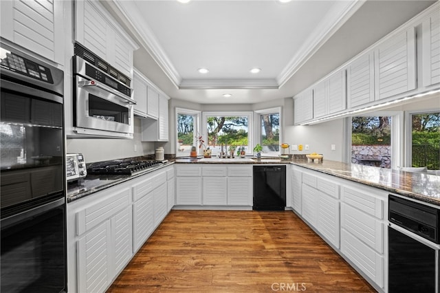 kitchen with ornamental molding, wood finished floors, white cabinets, black appliances, and a raised ceiling