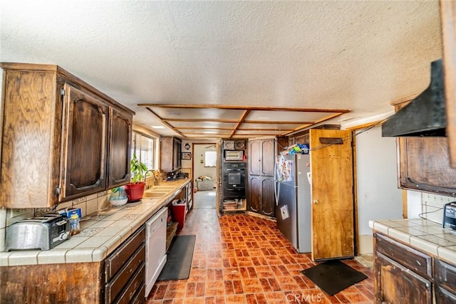 kitchen featuring a sink, black oven, tile counters, freestanding refrigerator, and dishwasher