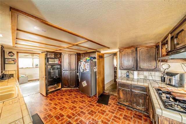 kitchen with tile countertops, decorative backsplash, freestanding refrigerator, gas cooktop, and black oven