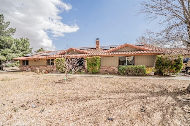 ranch-style home with brick siding, a tile roof, a chimney, and roof mounted solar panels