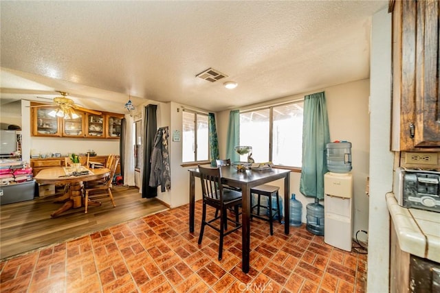 dining space with brick floor, visible vents, ceiling fan, and a textured ceiling