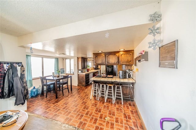 kitchen featuring brick floor, tile countertops, a breakfast bar area, a textured ceiling, and a peninsula