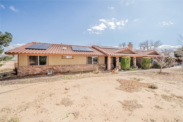 view of front of property featuring a tiled roof, brick siding, a chimney, and solar panels