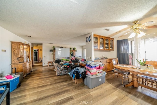 interior space featuring light wood-type flooring, ceiling fan, visible vents, and a textured ceiling