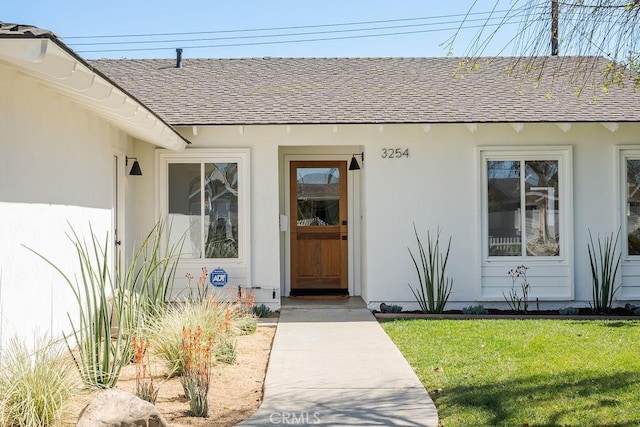 doorway to property featuring roof with shingles and a lawn