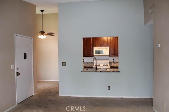 kitchen featuring carpet, a high ceiling, a sink, ceiling fan, and white appliances