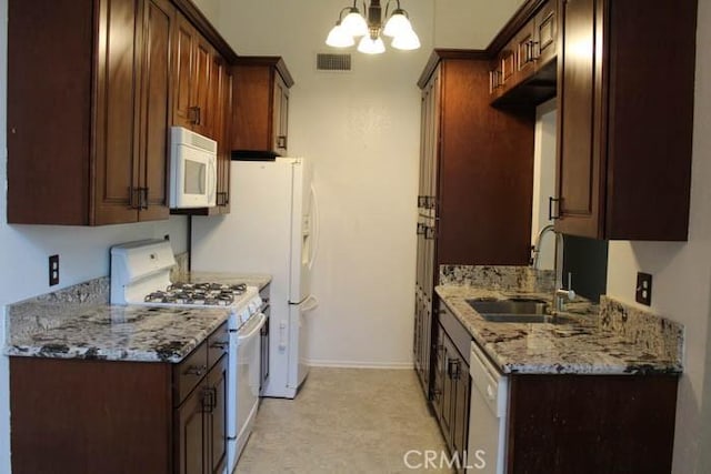 kitchen featuring white appliances, visible vents, light stone countertops, an inviting chandelier, and a sink