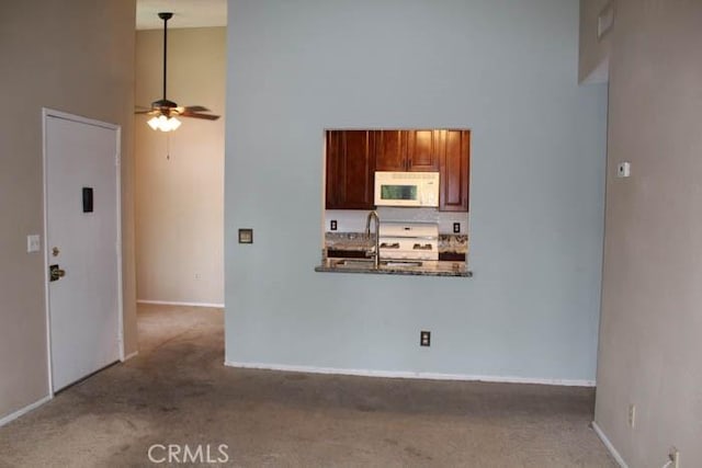 kitchen featuring carpet, a high ceiling, white microwave, ceiling fan, and a sink