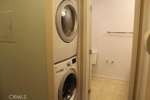 washroom with laundry area, baseboards, stacked washer / drying machine, and a textured wall