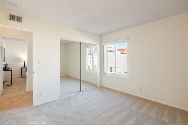 unfurnished bedroom with visible vents, baseboards, light colored carpet, a closet, and a textured ceiling