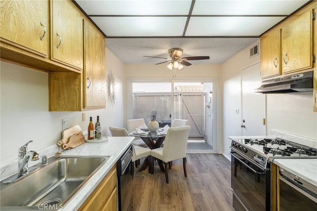 kitchen featuring wood finished floors, a sink, black dishwasher, gas range oven, and under cabinet range hood