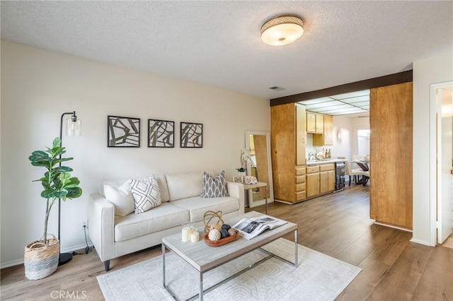 living room featuring visible vents, light wood-style flooring, a textured ceiling, and baseboards