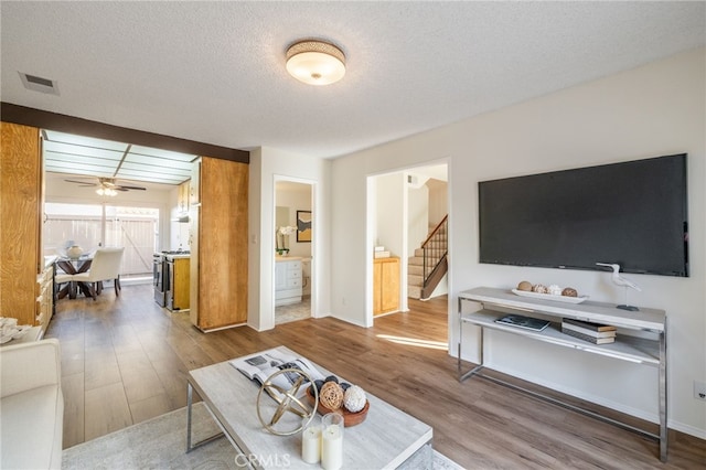 living area featuring visible vents, a ceiling fan, a textured ceiling, wood finished floors, and stairway