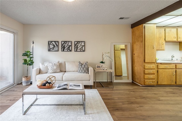 living area featuring light wood-type flooring, a textured ceiling, and visible vents