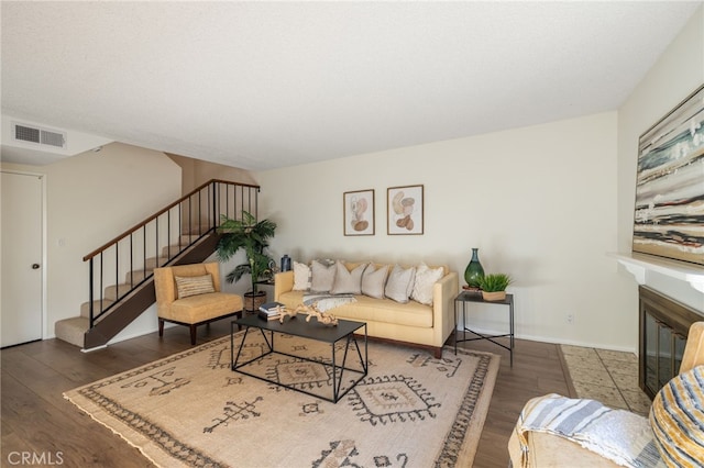 living area featuring visible vents, baseboards, stairway, wood finished floors, and a glass covered fireplace