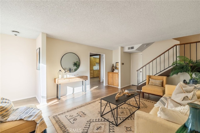 living room with stairway, wood finished floors, visible vents, and a textured ceiling