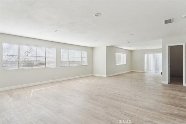 empty room featuring light wood-type flooring, visible vents, and baseboards